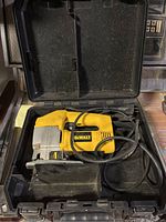 Dewalt sabre saw in black plastic carrying case, showing top and handle side with visible power cord.