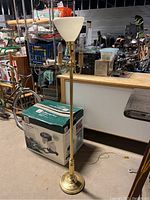 Full view of the vintage brass floor lamp standing on the floor showing the large milkglass shade and brass vertical shaft with a round base.