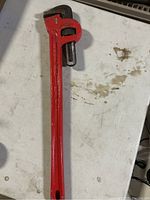 Red Swordfish pipe wrench on white surface showing full length and adjustable jaw.