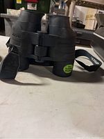 Front view of black Jason binoculars with dual eyepieces and carrying strap, showing sticker 'For Eyeglass Wearers'.