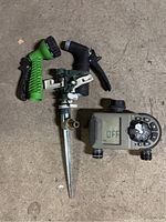 Photo of sprinkler head, two hose nozzles, and irrigation timer on floor