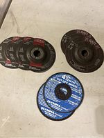 Seven metal cutting wheels arranged on a flat surface. Three Sait wheels with red text, three Sait wheels with purple text, one blue Olympia Tools cutting wheel at the front.