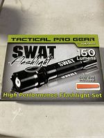 Box showing SWAT Flashlight Tactical Pro Gear packaging with 150 lumens and safety wand included