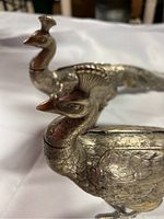 Close-up of two silver metal pheasant figurines showing heads, necks, and detailed feather engraving