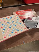 Two vintage Scrabble games laid out including one board and red box with letter tiles in a black bag, tile racks and instructions.