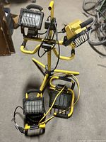 Overview of all four yellow work lights included in the lot, showing one large tripod mounted light and three smaller portable lights placed on the floor.