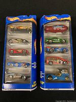 Front view of two unopened Hot Wheels gift packs, each containing five die-cast cars in clear plastic packaging, with blue cardboard backing featuring Hot Wheels logo and flames.