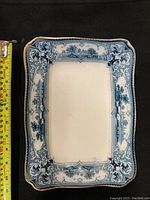 Close-up of one ceramic tray showing detailed blue and white "Verona" pattern with a measuring tape beside it indicating size approximately 11 inches long