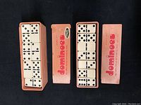 Two pink boxes labeled 'donalocs' containing 28 domino pieces each, pieces are visible with black pips and metal spinners.