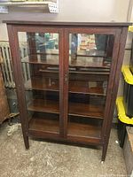 Front view of the dark wood glass cabinet showing two front doors and three interior shelves
