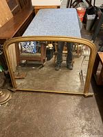 Front view of the large antique mirror with wooden frame resting against a table and floor, showing frame color and condition