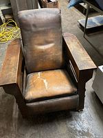 Front view of recliner showing padded back and seat upholstery with wear and cracking and oak armrests.