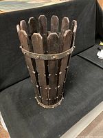 Front side view of the wooden umbrella and cane holder basket showcasing vertical wooden slats and metal bands with signs of wear.