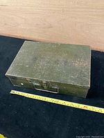Closed green painted WWII metal supply box with metal latch and handle, tape measure showing size.