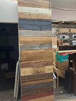 Photo showing multicoloured barn board panel vertically displayed in a workshop/storage area, various wood tones and textures visible.