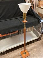 Full view of floor lamp standing on concrete floor showing white conical glass shade and slender wood and brass body.