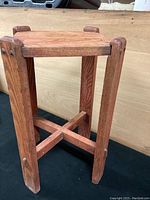 Left angled view of oak plant stand showing square top and cross brace with mostly removed red paint