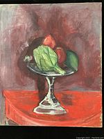 Oil painting still life showing artichoke, apples, and avocado arranged on a silver pedestal bowl on a red surface with a dark red background.