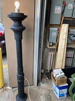 Full view of the outdoor pole lamp standing approx 5 feet tall showing black metal post with exposed light bulb on top