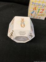 Photo of the bottom of the hexagonal ceramic coin bank showing Peter Rabbit illustration, Wedgwood branding, copyright 1971, 'Made in England', and signature 'Lord Wedgwood 2003'.