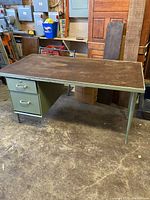 Full view of steel table with drawer unit on one side, worn dark top surface, green frame and tubular legs.