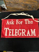 Front view of vintage red apron with large white text advertising Telegram service.