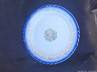 Top view of vintage plate showing white center with floral design and blue rim with gold trim
