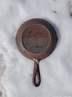 Bottom side of the cast iron pan showing the overall shape and handle in a snowy outdoor setting.