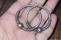 Pair of large silver hoop earrings with tribal details and central bead, placed on palm for scale.