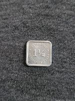 Photo showing one side of the square metal coin token with 'RETAILERS CORPORATION TOKEN 1 1/2' embossed.