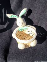 Front view of the small vintage woven Easter basket with the plush bunny attached showing the light green ears and bow.