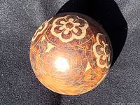 Side view of the hand-carved clay ball showing floral carved patterns on a glossy finish.
