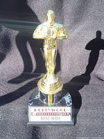 Photo of a gold-colored statuette trophy approximately 10 inches tall with a plaque that reads 'Hollywood Best Wife'