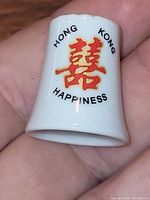 Close up of the ceramic thimble showing the red double happiness character and text 'Hong Kong Happiness'.