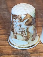 Porcelain thimble with kitten and puppy illustration on a wooden surface.