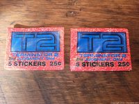 Two sealed vintage Topps Terminator 2 Judgment Day trading card sticker packs shown on wooden surface, front showing T2 and 5 stickers text with 25 cent price.