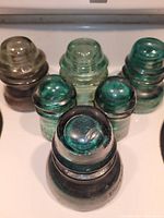 Photo showing six vintage glass insulators in aqua, teal, and clear shades, arranged close together to highlight color and shape.