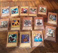 15 older Yu-Gi-Oh! trading cards arranged on a wooden surface showing front artwork and names.
