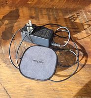 Photo of Mophie wireless charging pad and power adapter on wooden surface in natural light.