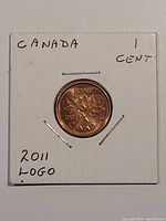 Photo of 2011 Canadian 1 cent coin in white cardboard 2-inch holder, shows 3 maple leaves design.