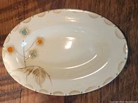 Oval porcelain mini platter placed on wood surface, showing scalloped edge and painted floral design.