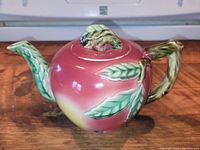 Front view of Moyott antique ceramic teapot with pink and green leaf decorations on the handle, spout, and lid.