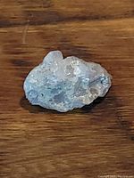 Close-up of a natural quartz crystal mineral specimen showing clear crystalline formations and an irregular shape on a wooden surface.