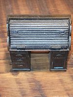 Front view of vintage pencil sharpener shaped like a roll top desk showing detailed drawers and textured roll top lid.