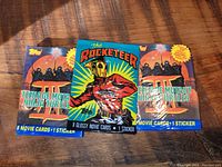 Photo shows three unopened vintage Topps movie card packs: two Teenage Mutant Ninja Turtles and one The Rocketeer in center.