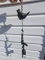 Wind chime showing black bird at top and hanging metal tubes and clapper beneath.
