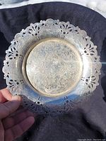 Top view of a circular silver plated wine bottle rest showing detailed floral engravings and an ornate pierced rim.