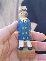 Front close-up of the carved wooden captain figurine showcasing details of the face, hat, coat, pipe, and base.