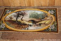 Full view of the rectangular area rug showing the detailed scenic design with bridge, water, trees, and floral border on wooden floor.