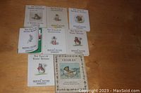 Photo of seven small Beatrix Potter books with white covers, placed on a wooden surface along with the book Charles by Lloyd Mask Skemp.